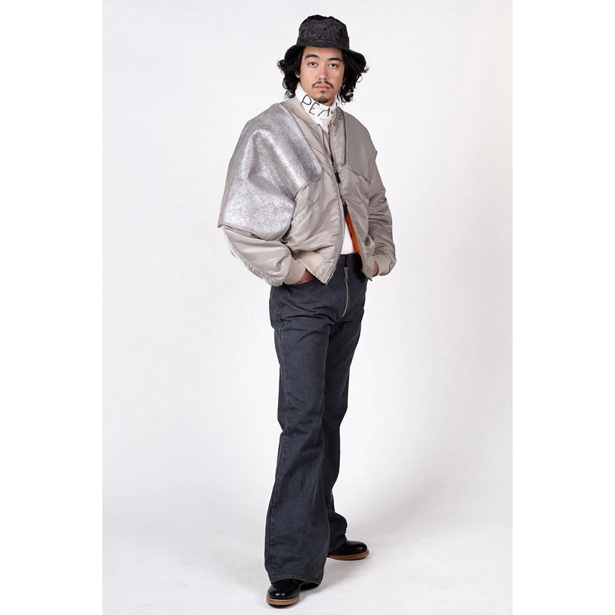 Person wearing a silver jacket and dark pants on a white background